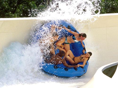A group of people in a blue inner tube splashes down a water slide, surrounded by water and excitement.