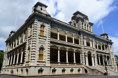 Historic building with ornate architecture, featuring large windows and a grand staircase, set against a blue sky.