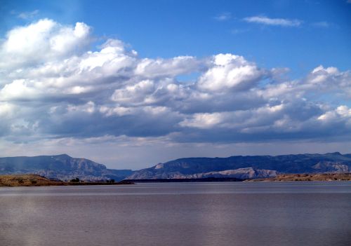 A serene lake surrounded by mountains under a blue sky with fluffy clouds.