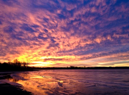 Vibrant sunset over a calm lake, with colorful clouds reflecting on the water's surface.