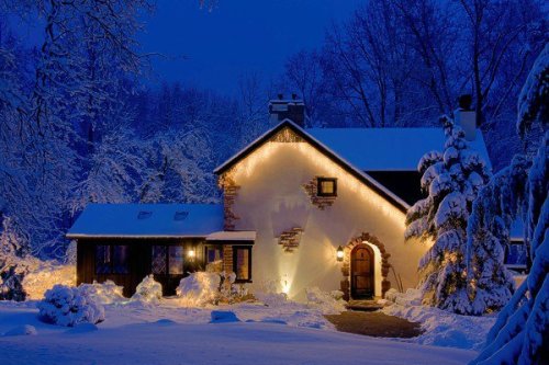 A cozy house adorned with warm lights, surrounded by snow-covered trees in a serene winter night.