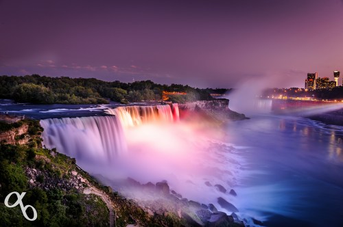 A vibrant view of Niagara Falls at dusk, illuminated by colorful lights, with mist rising over the water.