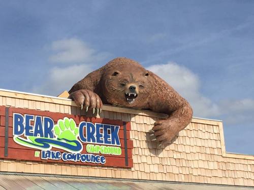 A large bear statue perched on the roof of Bear Creek Campground, with a blue sky in the background.