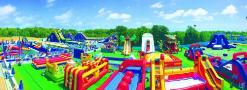 A vibrant outdoor inflatable park filled with various colorful bounce houses and slides under a clear blue sky.