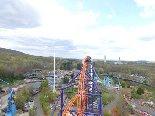 Aerial view of a theme park featuring roller coasters and green trees under a cloudy sky.