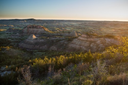A panoramic view of rolling hills and valleys at sunset, with lush greenery and rugged terrain under a clear sky.