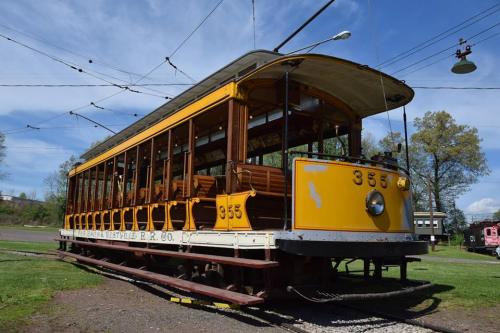 A vintage yellow streetcar with wooden benches, parked on tracks under a clear blue sky.