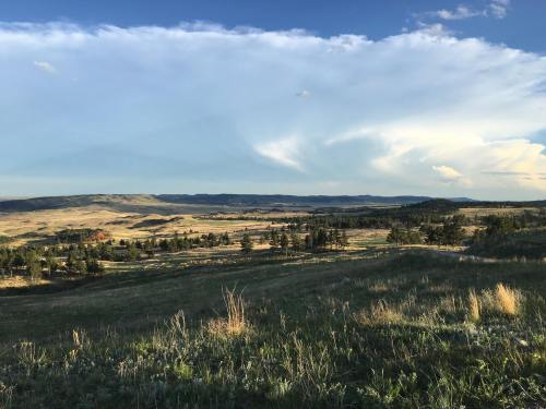 A scenic landscape featuring rolling hills, green fields, and a blue sky with wispy clouds.