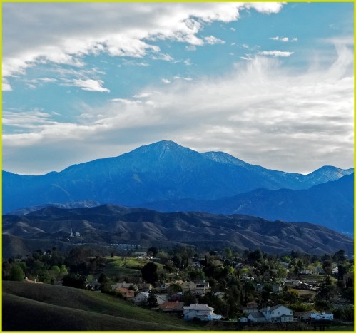 A scenic view of mountains under a cloudy sky, with rolling hills and a small town in the foreground.