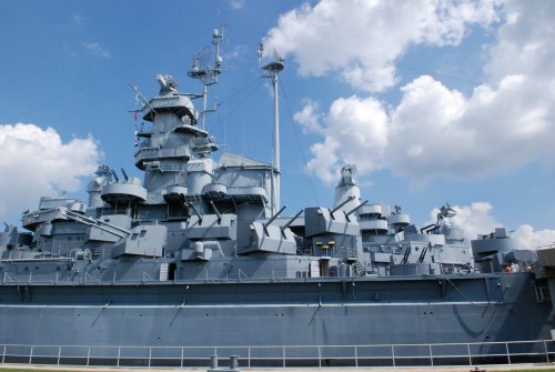 A large gray battleship docked under a blue sky with fluffy clouds.