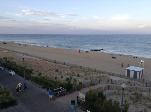 A serene beach scene with soft sand, gentle waves, and a few people enjoying the sunset along the shoreline.