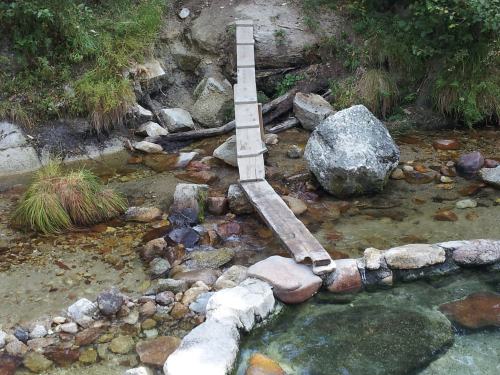 A wooden bridge spans a shallow stream, surrounded by rocks and greenery.
