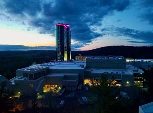 A city skyline at dusk featuring a tall building with pink lights and a mountainous backdrop.