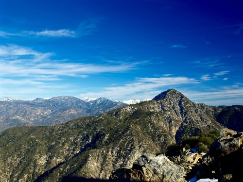 A panoramic view of snow-capped mountains under a clear blue sky, showcasing rugged terrain and distant peaks.