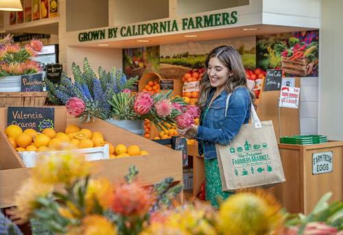 A woman smiles while selecting flowers at a vibrant farmers market filled with fresh produce and colorful blooms.