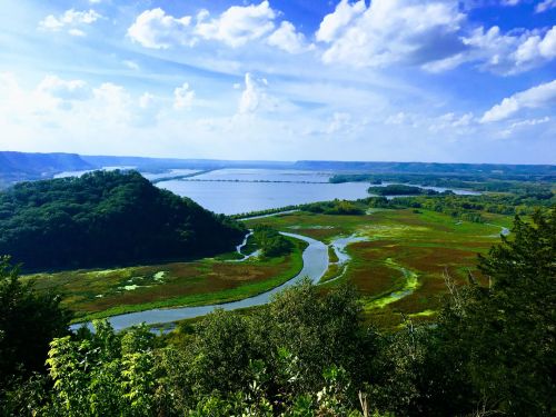 A scenic view of a river winding through lush green landscapes under a blue sky with fluffy clouds.