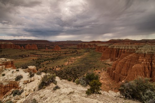 A dramatic landscape of red rock formations and green valleys under a cloudy sky.