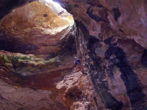 A person rappelling down a rocky cave with sunlight streaming in from above.
