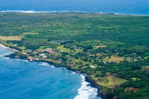 Aerial view of a lush green coastline with a small village and waves crashing on rocky shores.