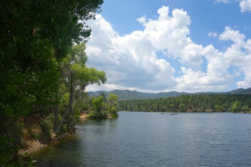 A serene lake surrounded by trees and mountains under a partly cloudy sky.