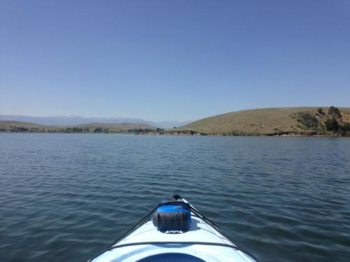 A view from a kayak on calm water, with hills and a clear blue sky in the background.