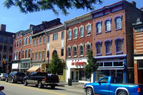 Historic buildings line a street, featuring colorful facades and shops under a clear blue sky.