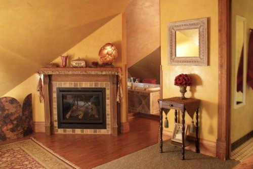 Cozy room with yellow walls, a fireplace, decorative table, and a glimpse of a bathroom in the background.