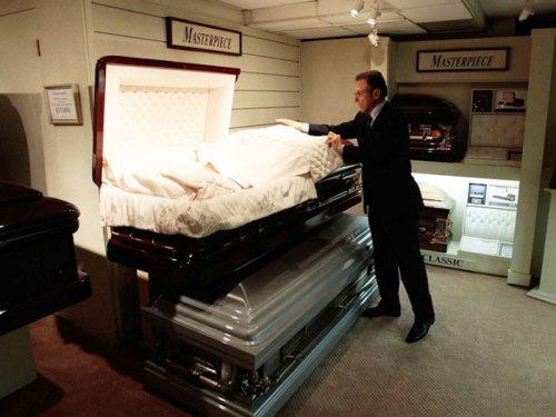 A man examines a casket in a display room, showcasing various coffin styles and designs.