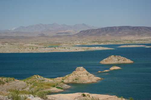 A serene landscape featuring a blue lake surrounded by arid land and distant mountains under a clear sky.