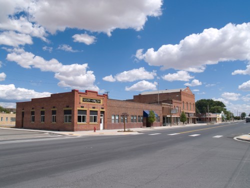 A small town street featuring brick buildings under a blue sky with fluffy clouds.