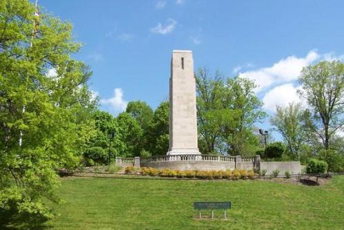 A tall stone monument surrounded by greenery under a blue sky with scattered clouds.