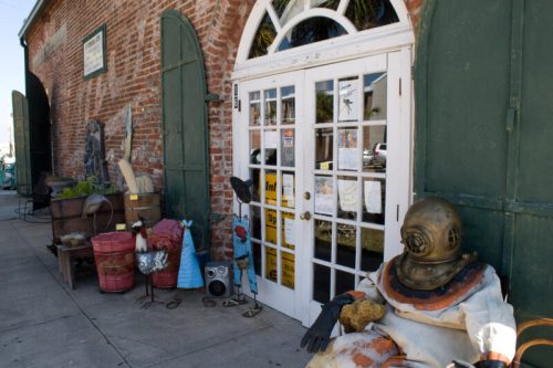 A vintage storefront with a large glass door, featuring quirky decorations and a diver statue sitting outside.