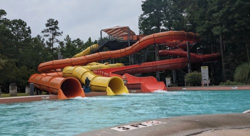 Colorful water slides twist and turn above a pool, surrounded by trees under a cloudy sky.