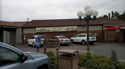 Exterior view of Moonlite Bar-B-Que, featuring a sign, parked cars, and a green lamp post in a cloudy setting.