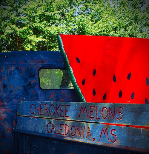 A vintage truck with a large painted watermelon and a sign reading "Cherokee Melons, Caledonia, MS."
