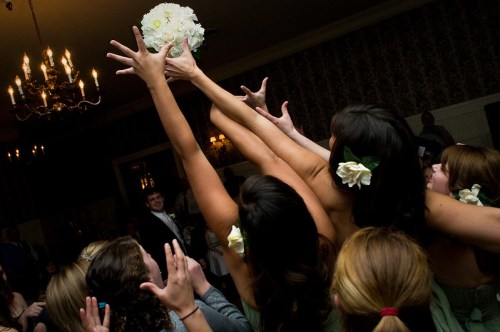 A group of women reaching for a bouquet during a wedding celebration, with excitement and floral decorations in their hair.