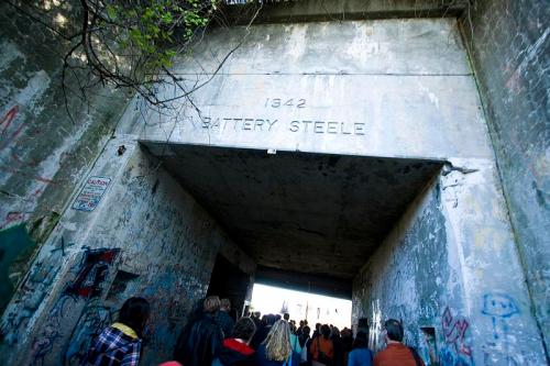 A group of people walking through a graffiti-covered tunnel with "1942 BATTERY STEELE" engraved above.