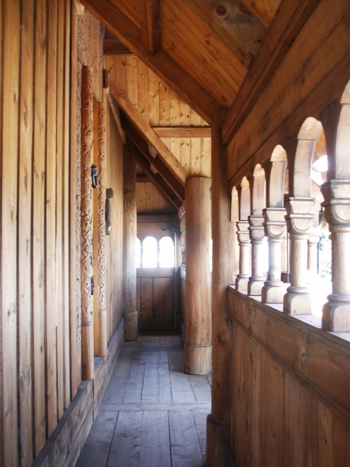 A wooden corridor with carved pillars and arches, featuring a warm, rustic design and natural light.