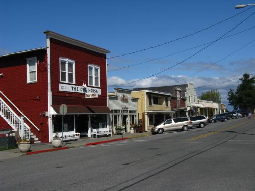 A quaint street scene featuring colorful buildings, including a red tavern, under a blue sky with scattered clouds.