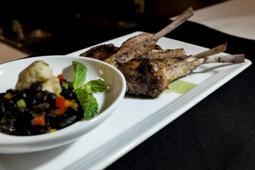Grilled lamb chops on a plate with black bean salad and a mint garnish.