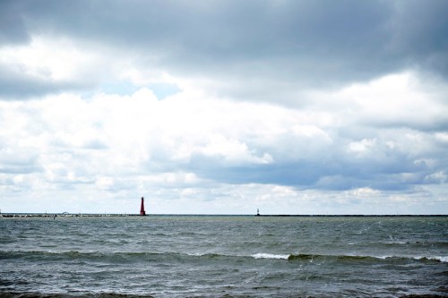A cloudy sky over a calm sea, featuring two distant lighthouses on the horizon.