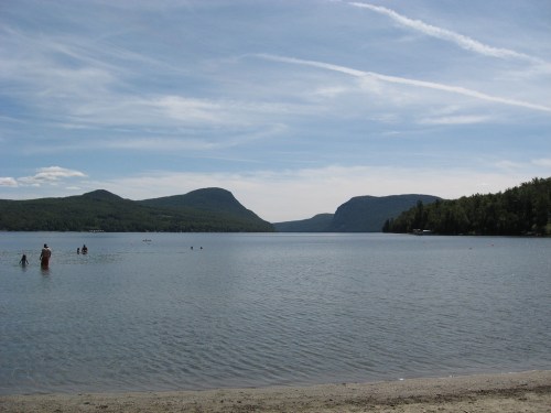 A serene lake surrounded by mountains, with people swimming and enjoying the water under a blue sky.