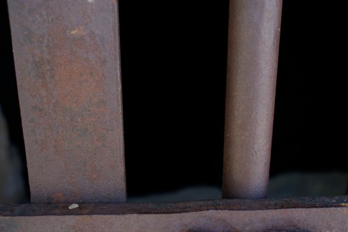 Close-up of rusty metal bars with a dark void behind them, suggesting confinement or an enclosed space.