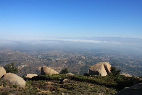 A panoramic view of rolling hills and valleys under a clear blue sky, with large boulders in the foreground.