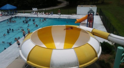 A colorful water slide overlooks a busy swimming pool filled with people enjoying a sunny day.
