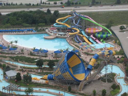 Aerial view of a water park featuring colorful slides, a large pool, and a lazy river surrounded by greenery.