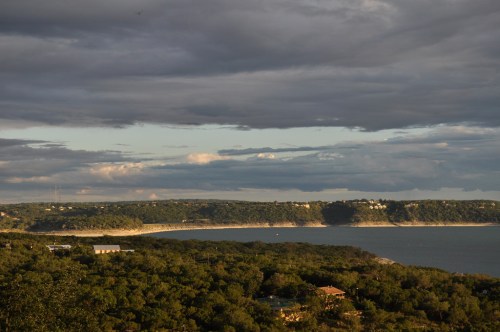 A scenic view of a coastline with lush greenery, under a cloudy sky reflecting soft sunlight.