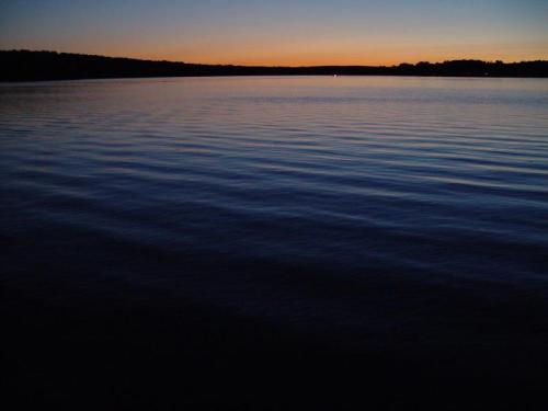 A calm lake at dusk, reflecting soft hues of blue and orange in the water under a twilight sky.