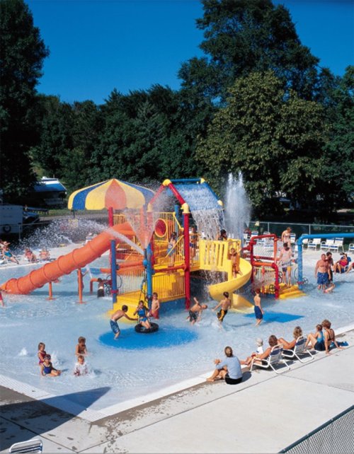 A vibrant water park with slides, splash pads, and children playing in the pool under a clear blue sky.