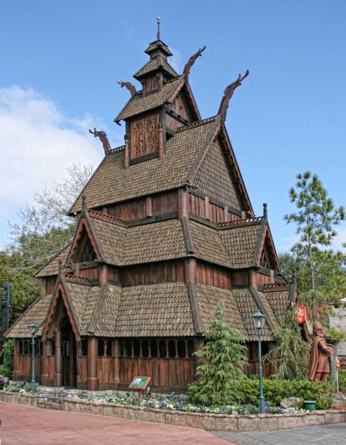 A wooden structure with a steep, tiered roof and decorative dragon heads, surrounded by greenery and blue sky.